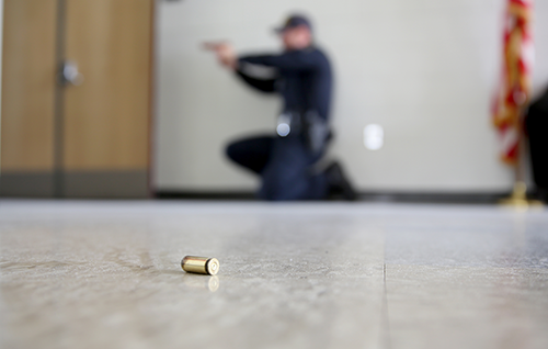 Active shooter exercise. Bullet in foreground and law enforcement officer with a gun in the background.